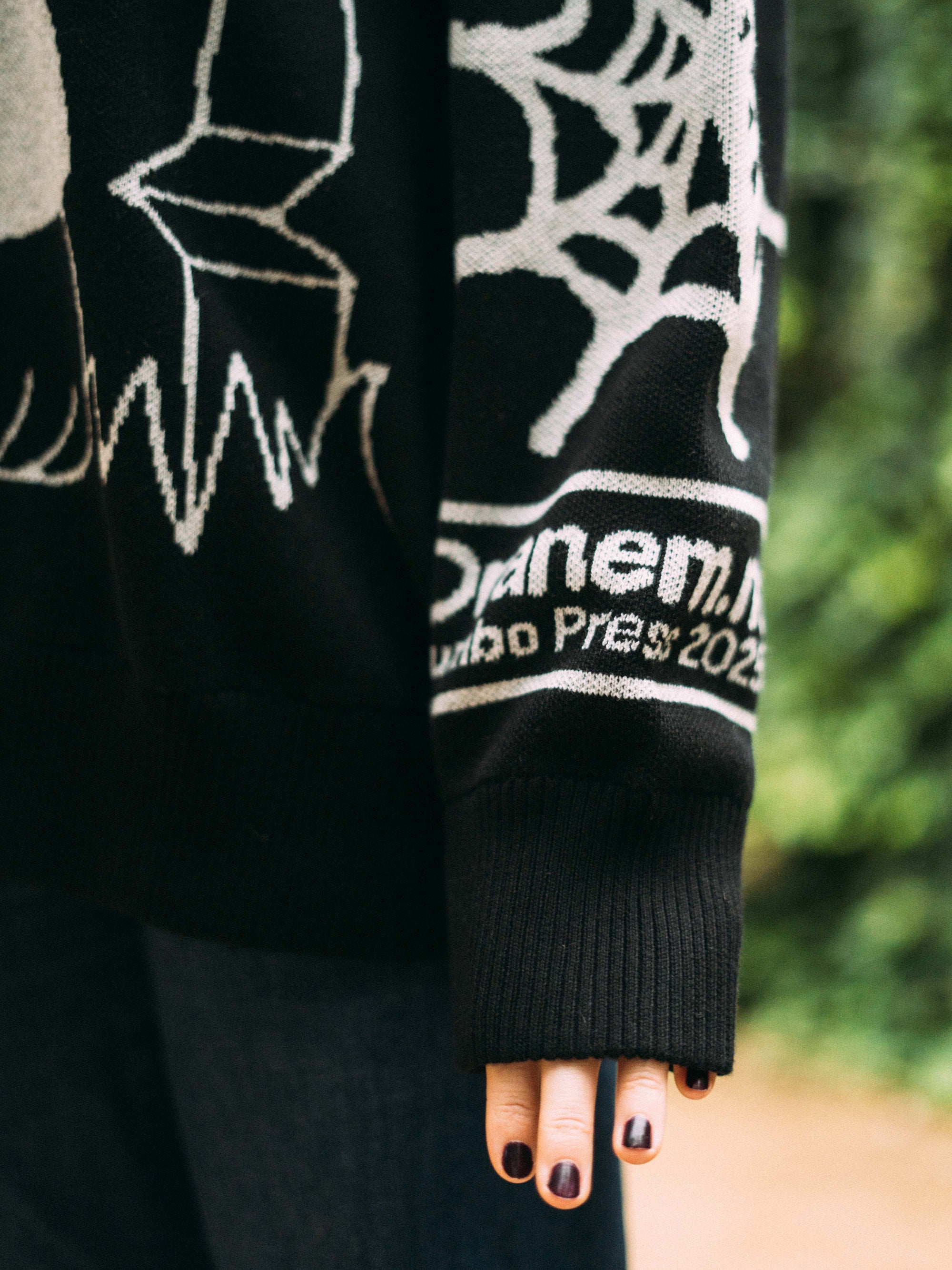 Black sweater with white designs and text, worn by a person.